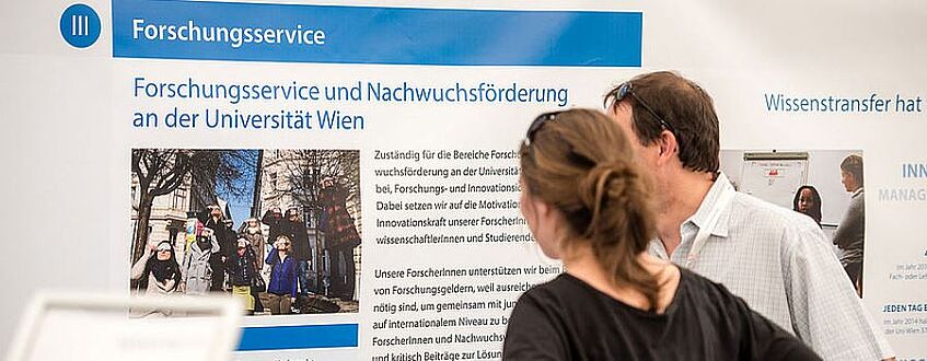 2 persons are reading a poster about research and career development at the University of Vienna
